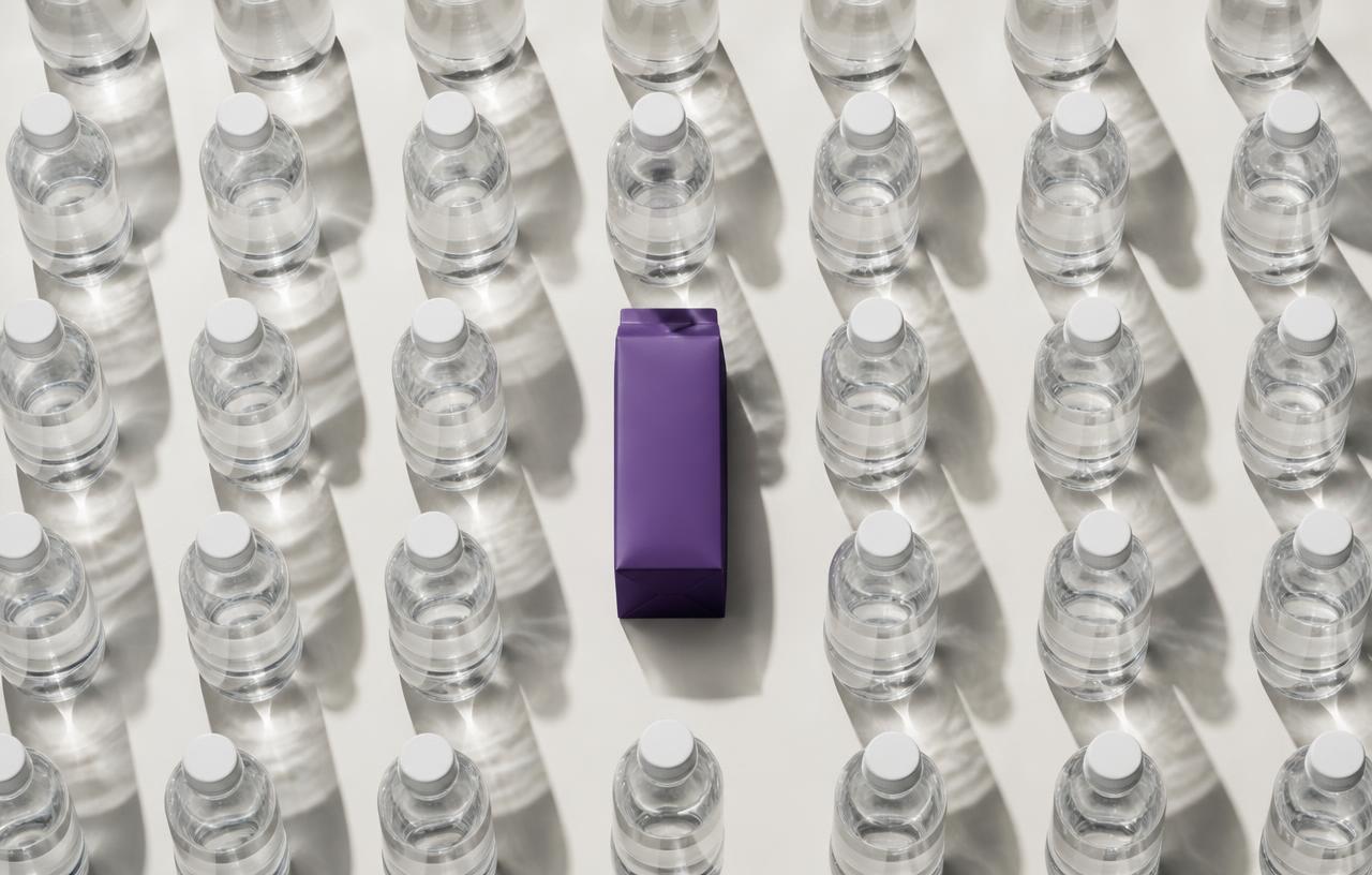 Hilera de botellas de agua en blanco y negro con un envase de cartón morado destacado en el centro